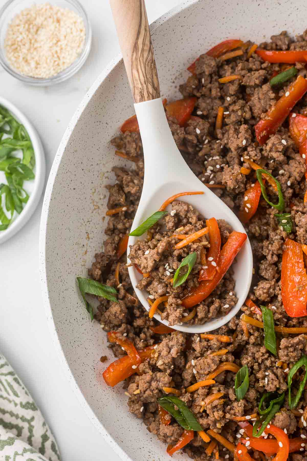 Ground beef teriyaki bowl filling in a white skillet with a spoon.