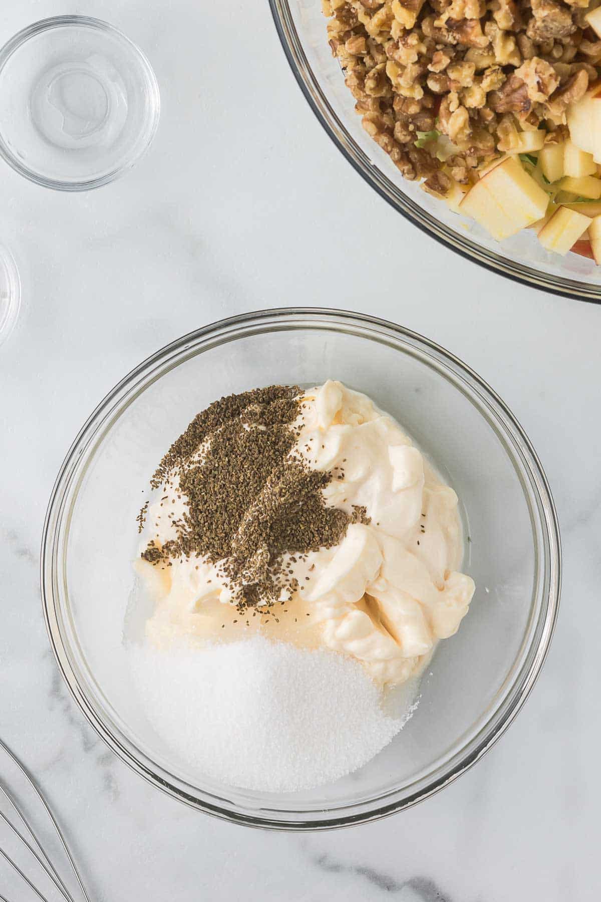 A glass bowl with mayonnaise, sugar, and pepper on a marble surface. 