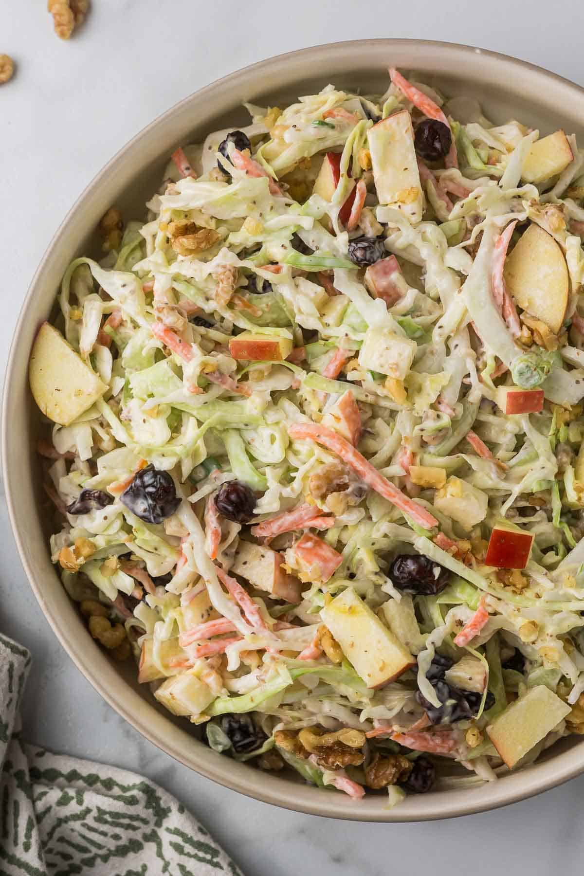 A bowl of coleslaw salad with shredded cabbage, carrots, apple slices, raisins, walnuts, and a creamy dressing. 