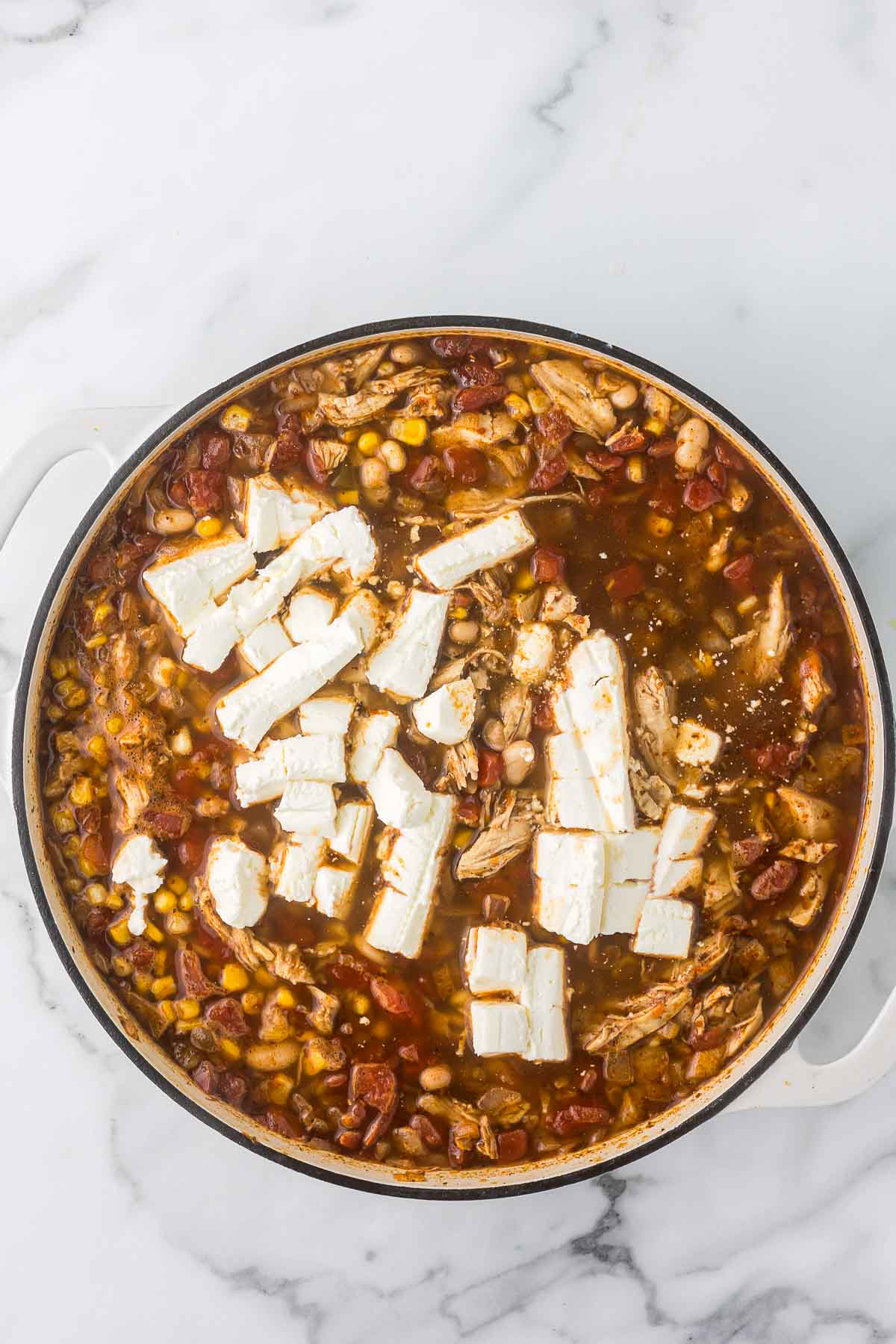 A large pot filled with beans, corn, shredded meat, and tomatoes, topped with chunks of white cheese.