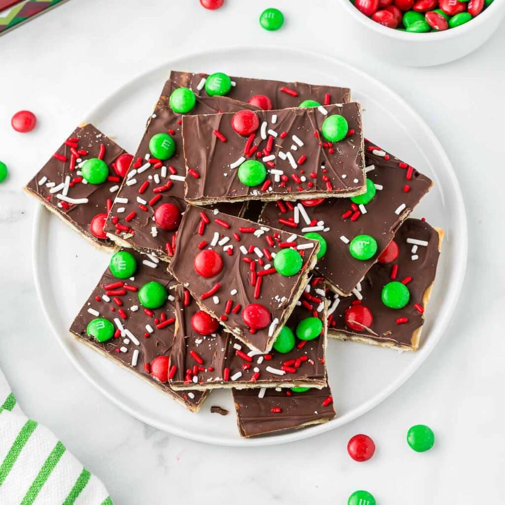 Saltine Toffee bark on a white plate with red and green chocolate candies and sprinkles.