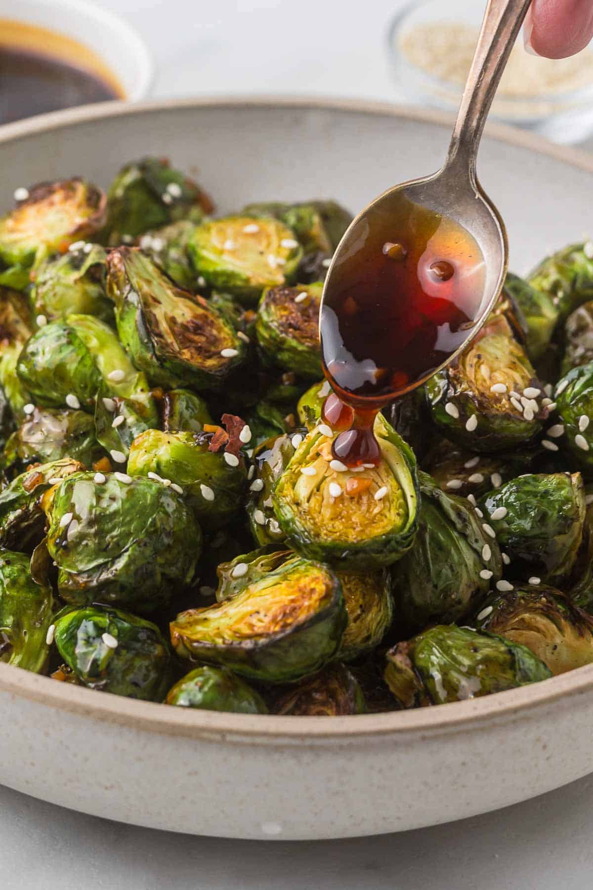 Brussels sprouts with teriyaki sauce being poured over the top with a spoon.