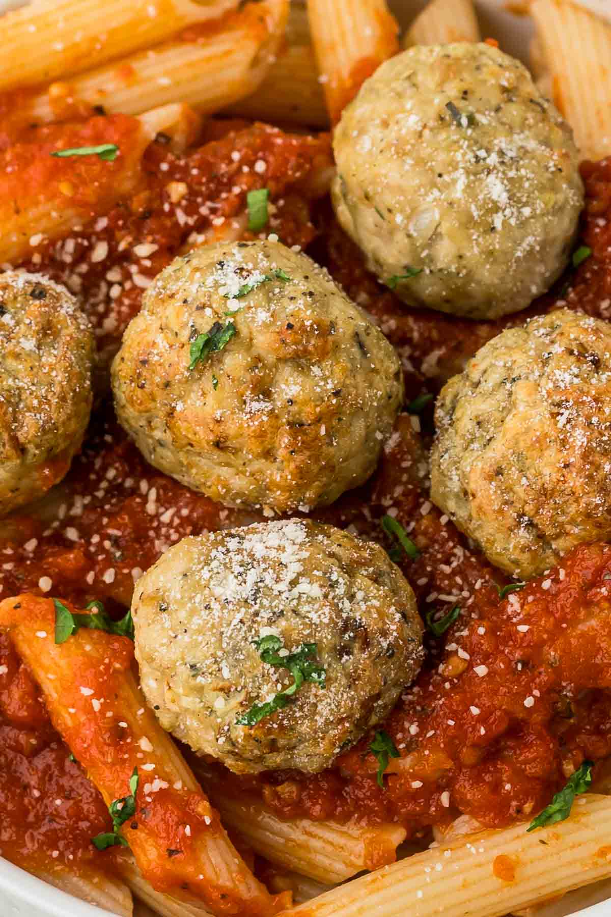 Chicken meatballs served over pasta with red sauce and sprinkled with fresh parsley.