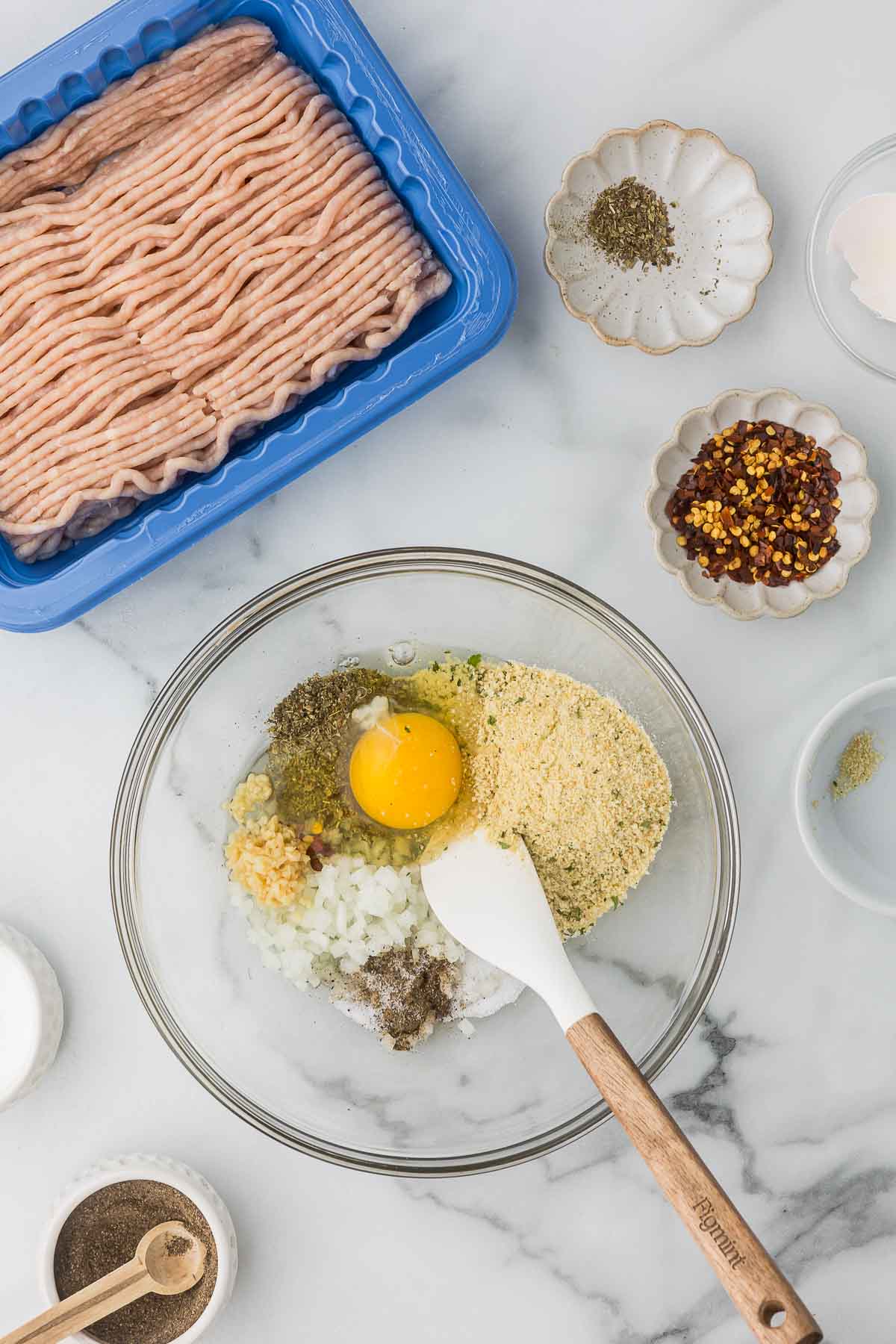 Egg, bread crumbs, garlic, onion and seasonings in a bowl to make chicken meatballs.