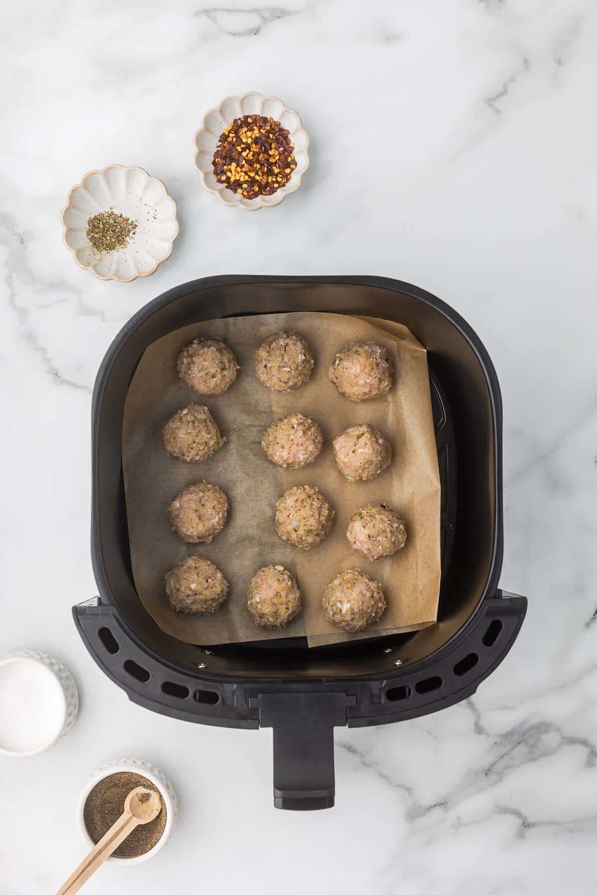 Air fryer basket with parchment paper and meatballs before they cook.