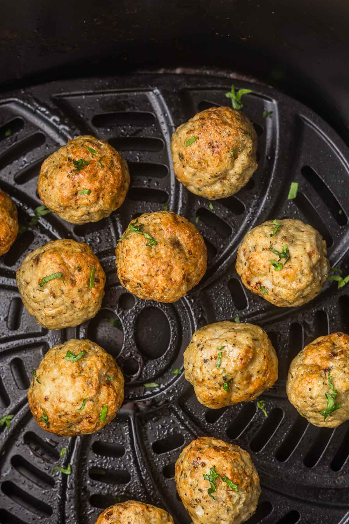 Chicken meatballs in an air fryer basket with fresh parsley after they have been cooked.