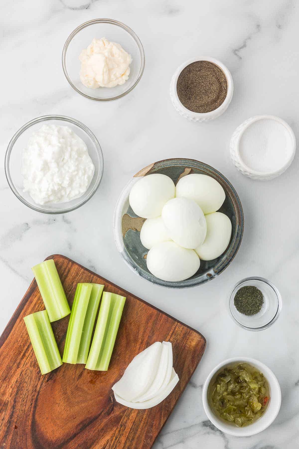 Ingredients to make cottage cheese egg salad including hard boiled eggs, salt and pepper, dill, celery, onion, cottage cheese, sweet relish, and mayo.