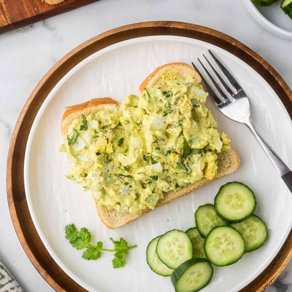 An open curried egg sandwich with cucumbers as a side.