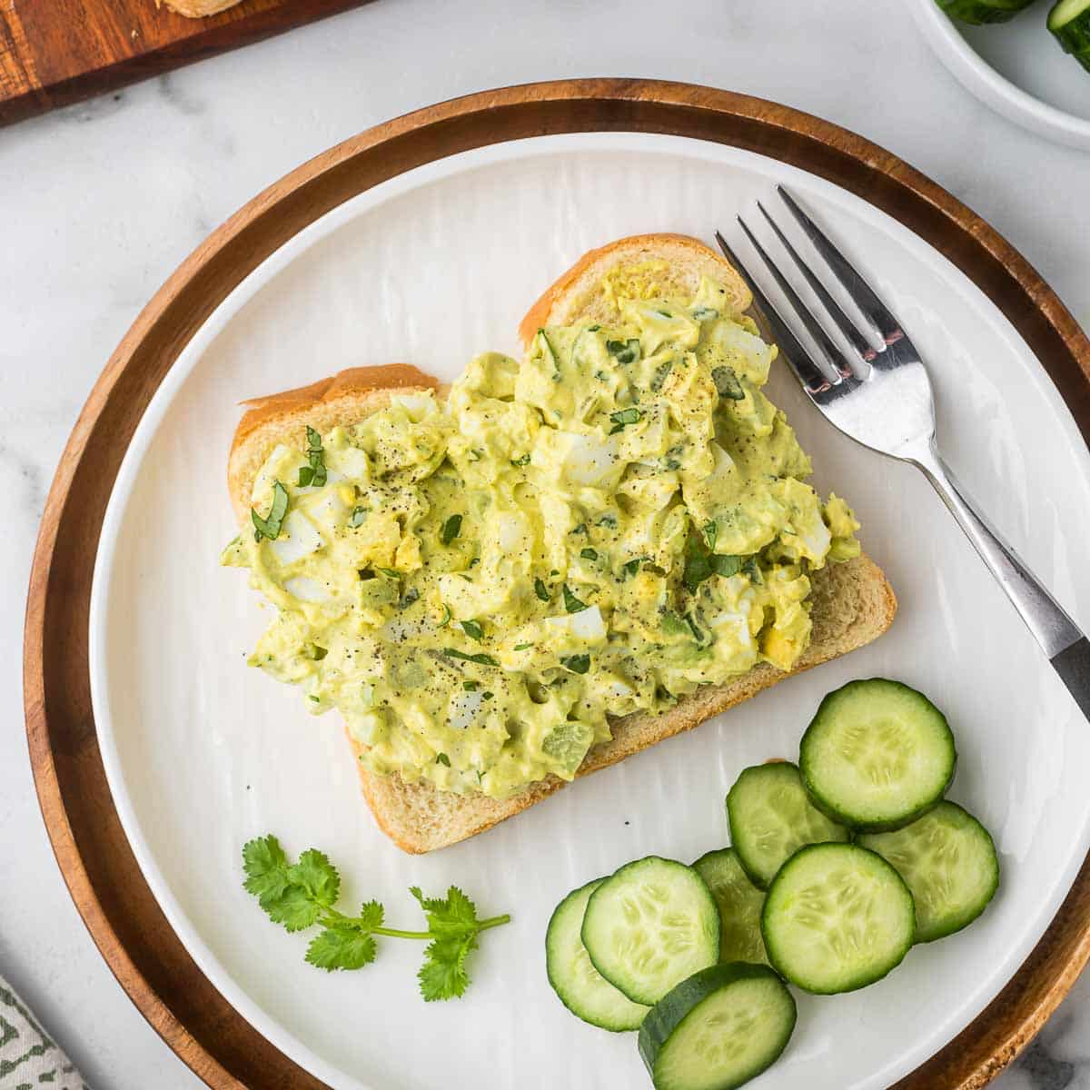 An open curried egg sandwich with cucumbers as a side.