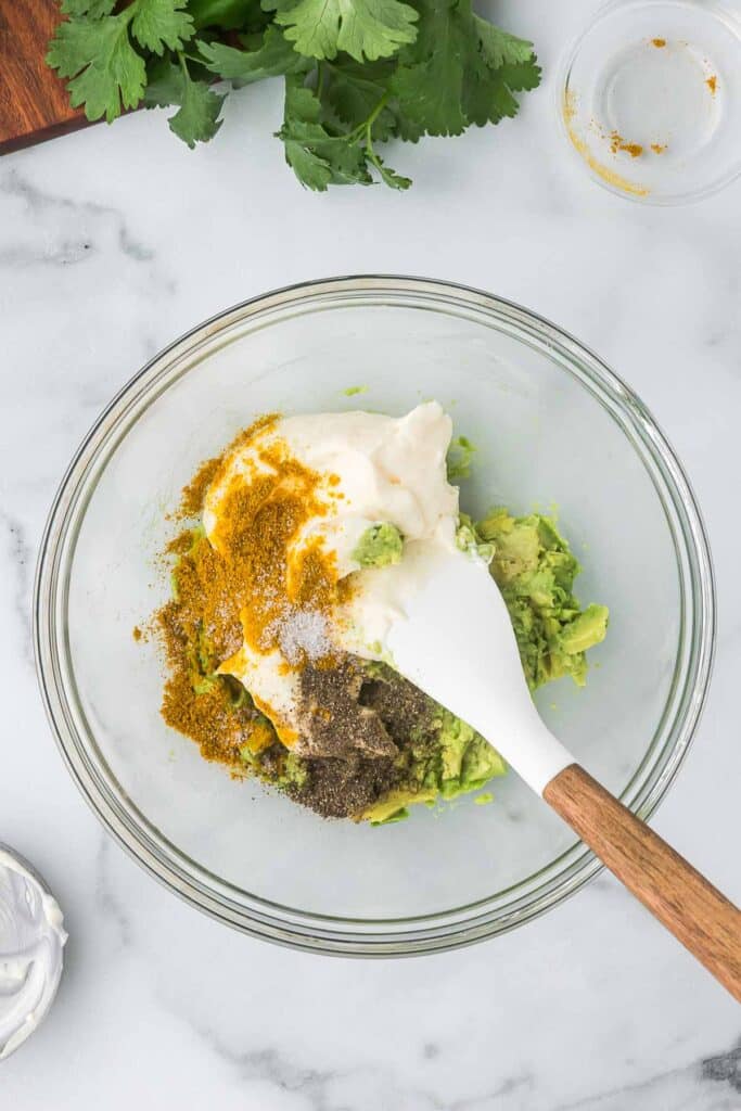 The dressing ingredients to make egg salad in a clear bowl with a spatula.