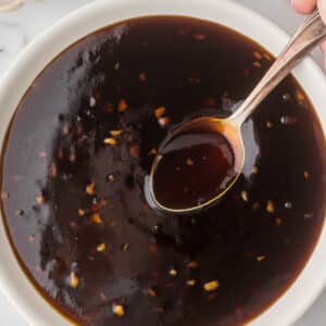 Homemade teriyaki sauce in a white bowl with a small serving spoon.