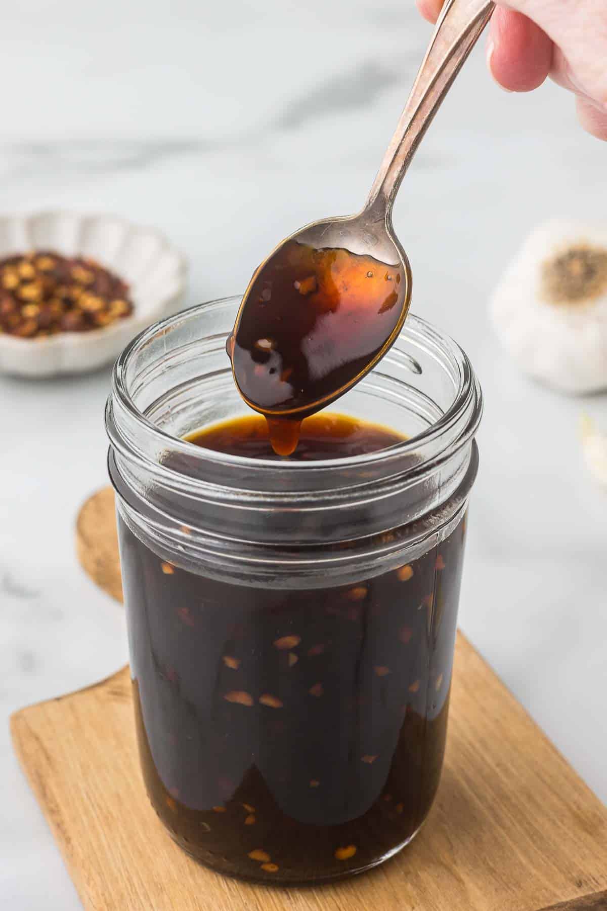 Teriyaki Sauce in a canning jar with a spoon sowing the thickness of the sauce.