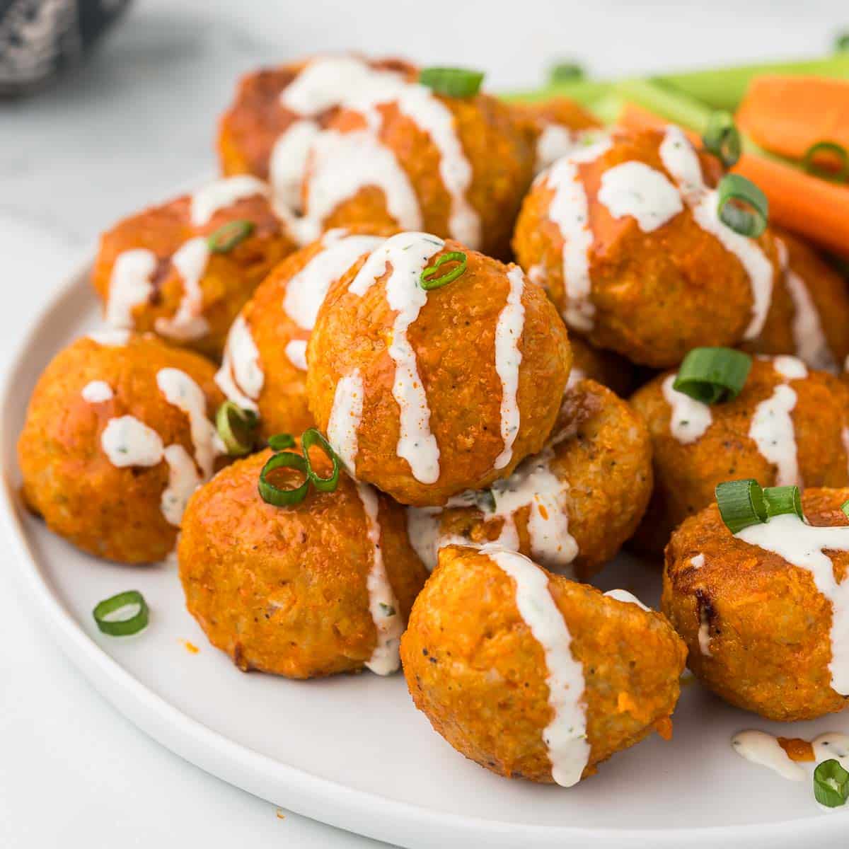 Buffalo Chicken Meatballs on a white platter with ranch dressing drizzled over them with green onions sprinkled over the top.