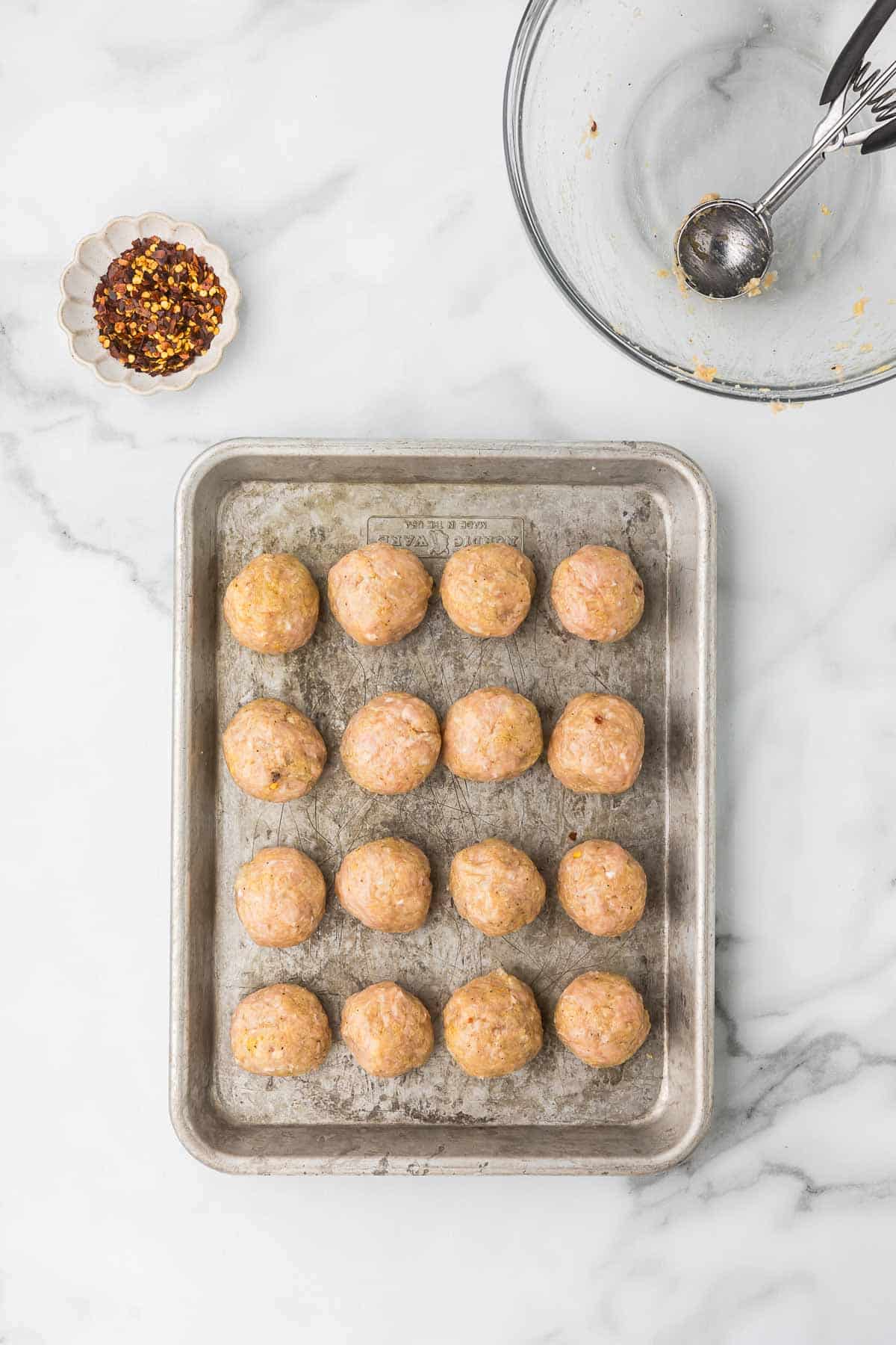 Raw chicken meatballs on a baking sheet before baking.