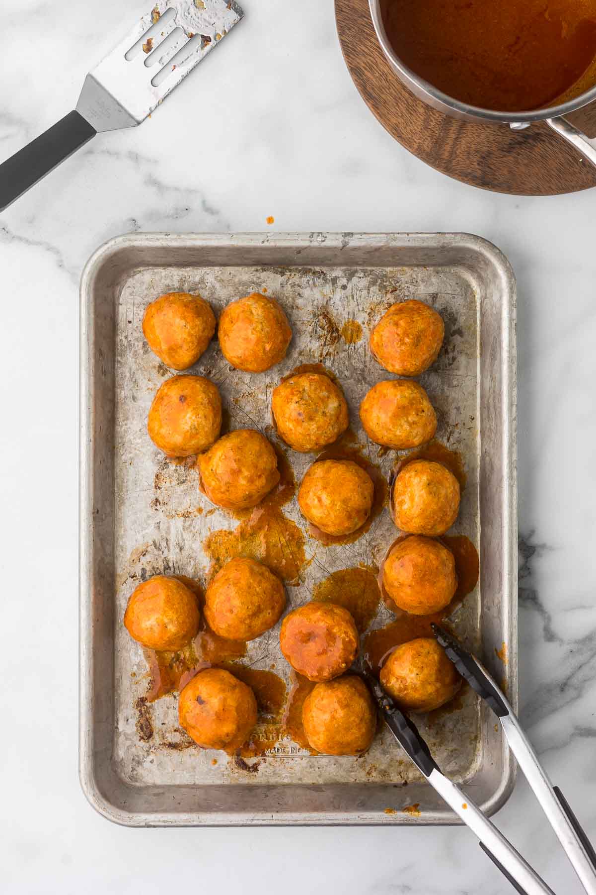 Buffalo Ground Chicken Meatballs on a baking sheet after they have been tossed with buffalo sauce.