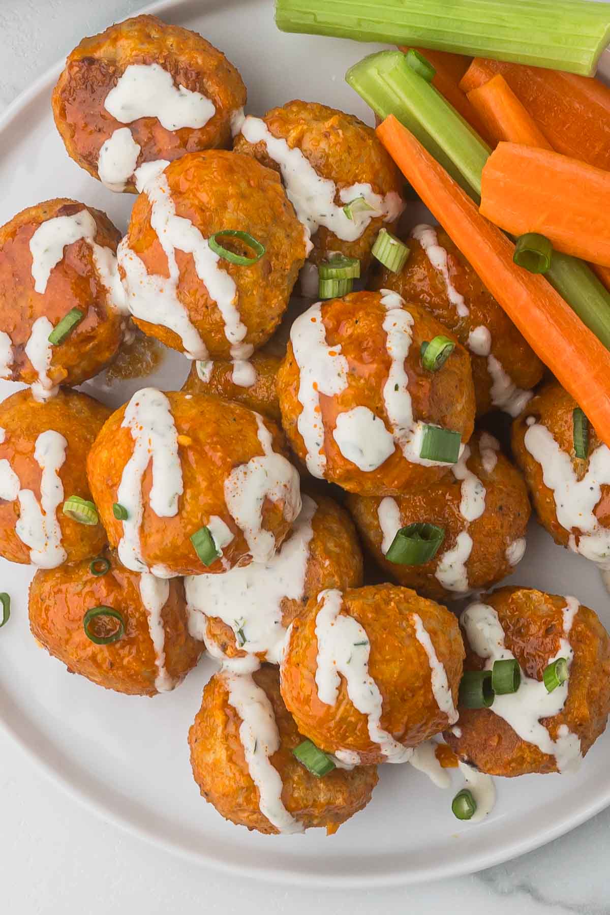 Buffalo Chicken Meatballs with ranch dressing drizzled and green onions sprinkled over the top. Carrot sticks and celery on the side.