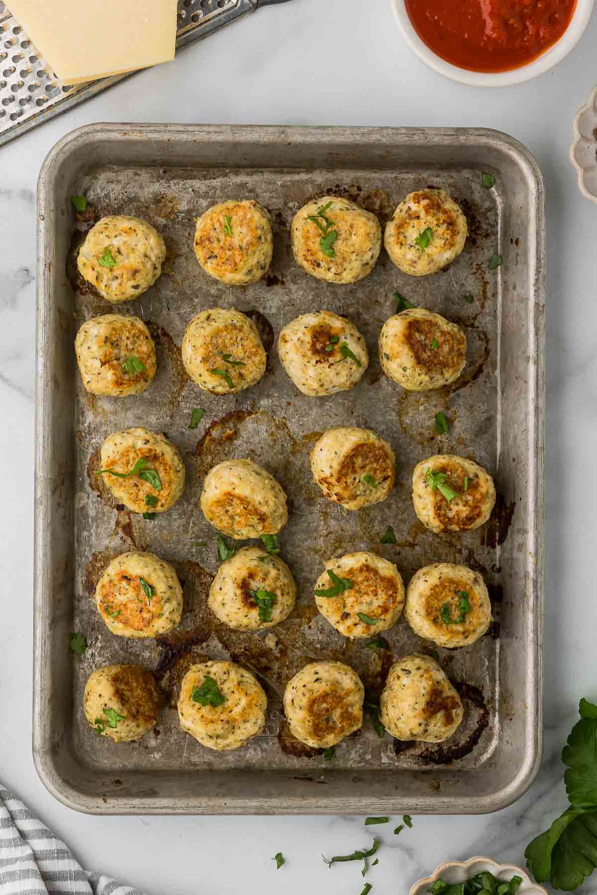 Baked chicken meatballs on a baking sheet with fresh parsley.