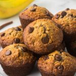 Oatmeal Banana Chocolate Chip Muffins on a plate with a couple bananas int he back ground.
