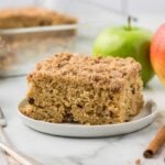 Applesauce Cinnamon Coffee Cake on a white plate with apples and more cake in the background.
