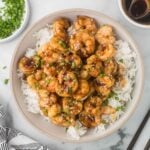 Shrimp Teriyaki on a bed of white rice with sesame seeds and green onions as garnish.
