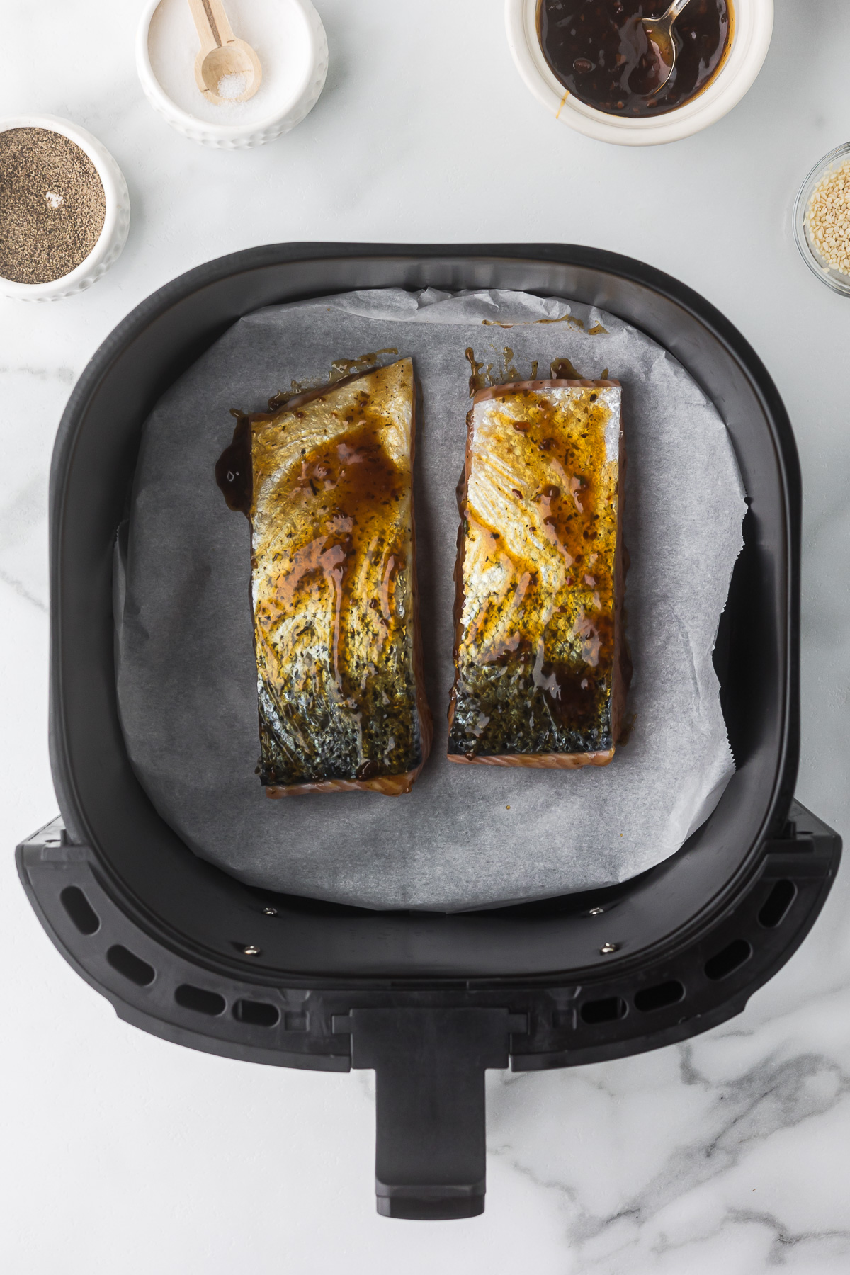 Air fryer salmon on parchment paper in an air fryer basket before being cooked.