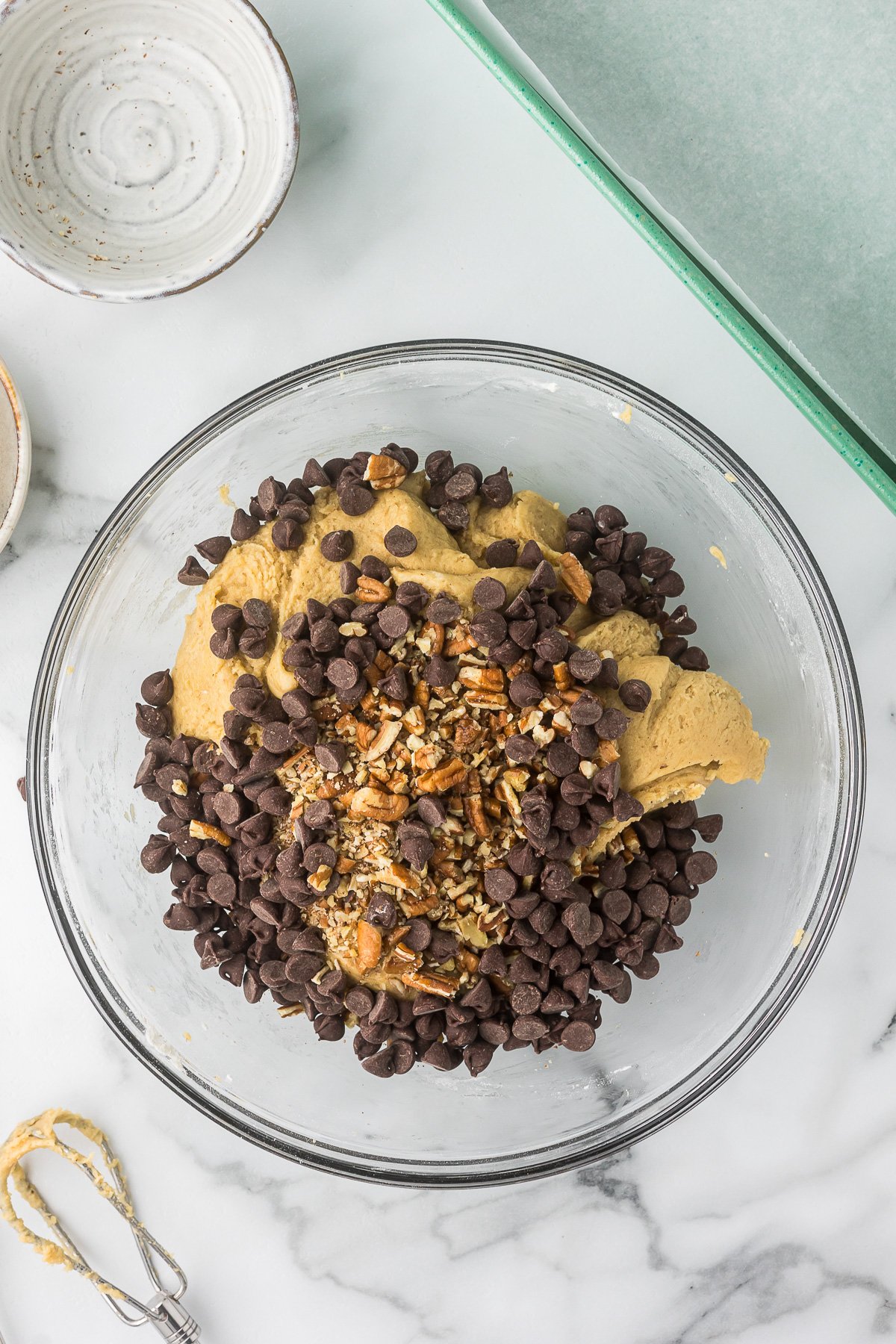 Chocolate chips and pecans being mixed into the cookie batter.