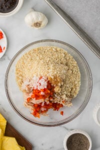 Ground chicken with egg, diced bell pepper and onion, and breadcrumbs in a bowl to make chicken burgers with teriyaki sauce.