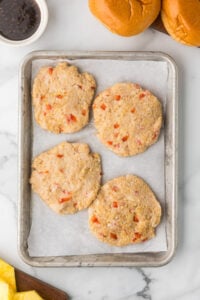Four formed chicken burgers on a sheet pan.