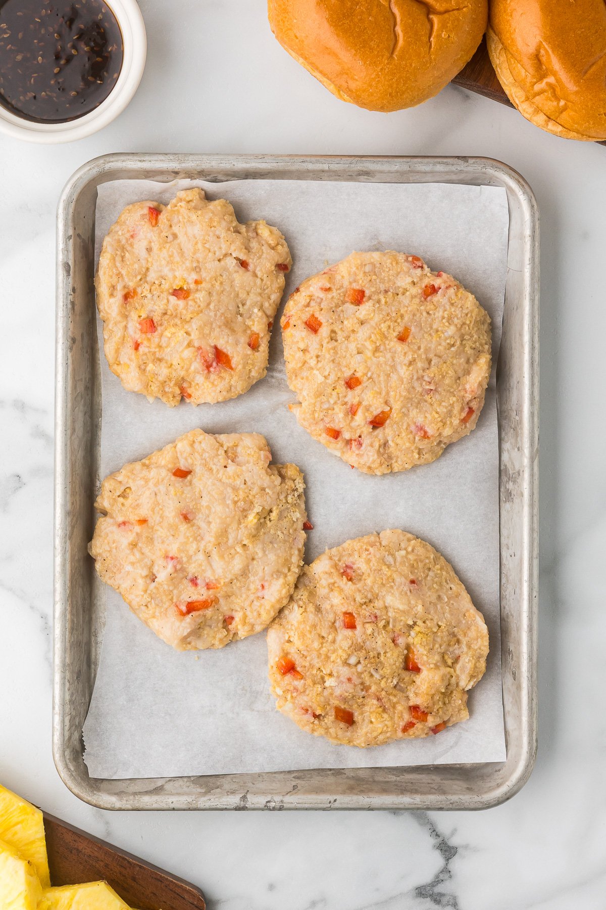 Four formed chicken burgers on a sheet pan. 