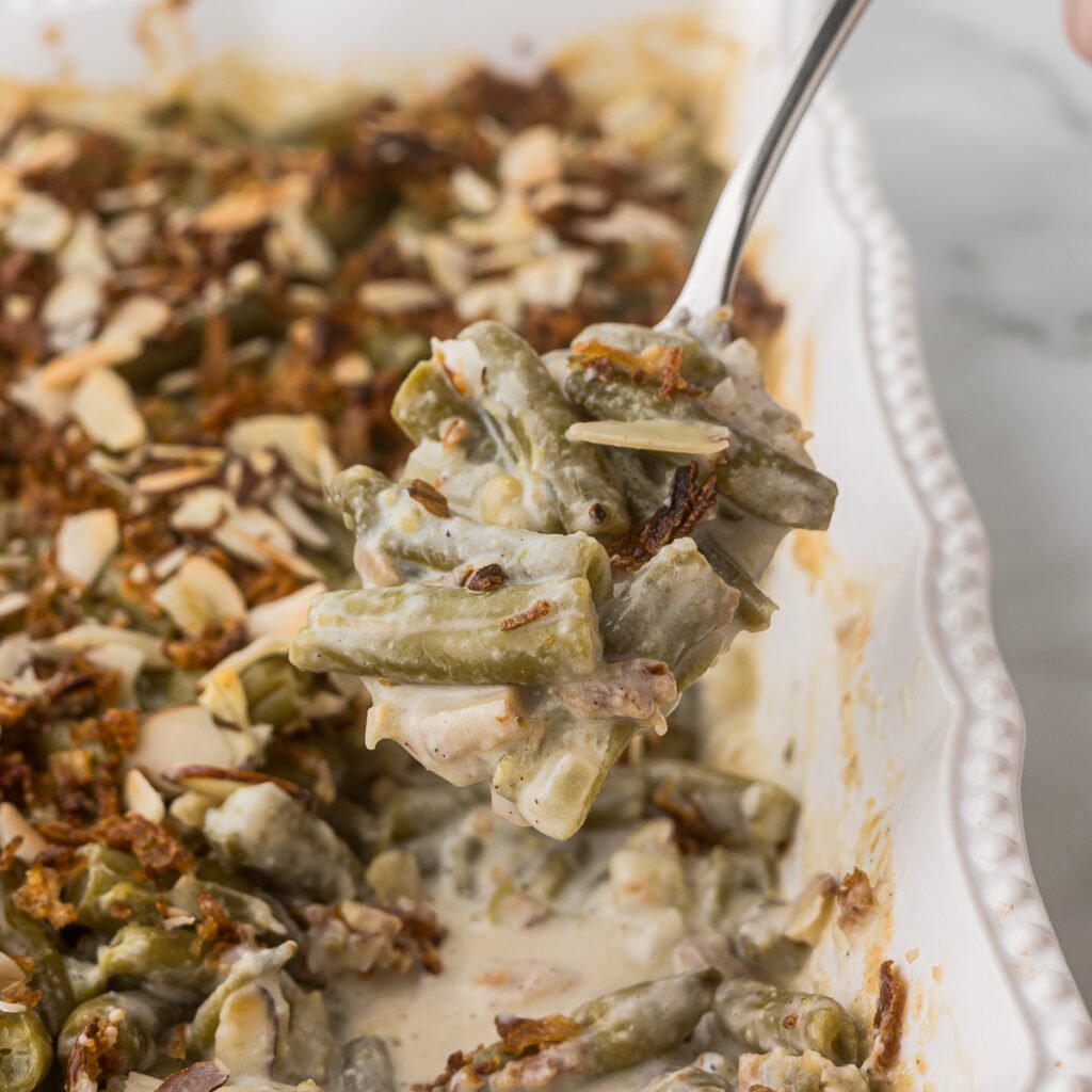 Green Bean Casserole in a white baking dish with a helping on a spoon.