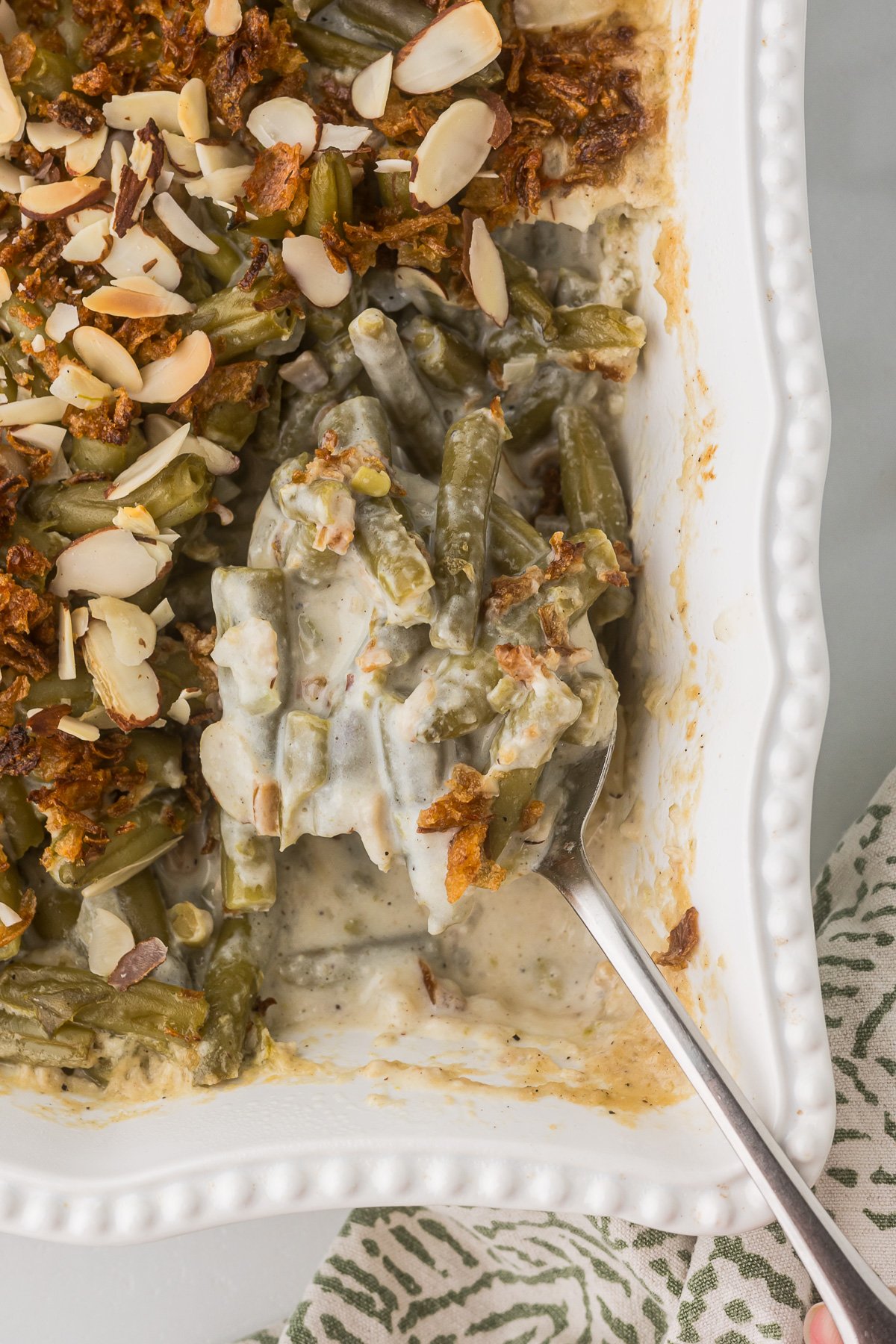 Cream Cheese Green Bean Casserole in a white casserole dish with a serving spoon.