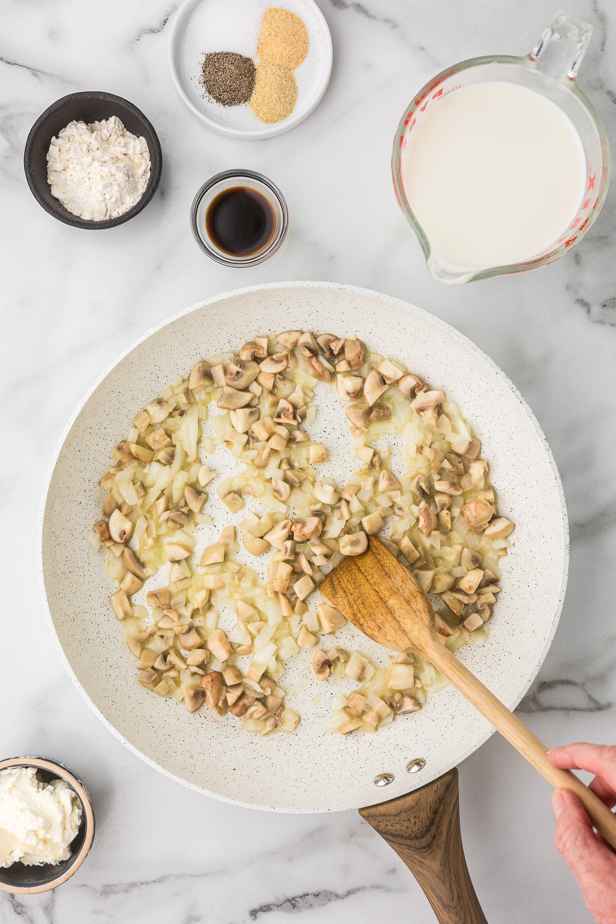Butter, onion and mushrooms in a pan with a wooden spoon.