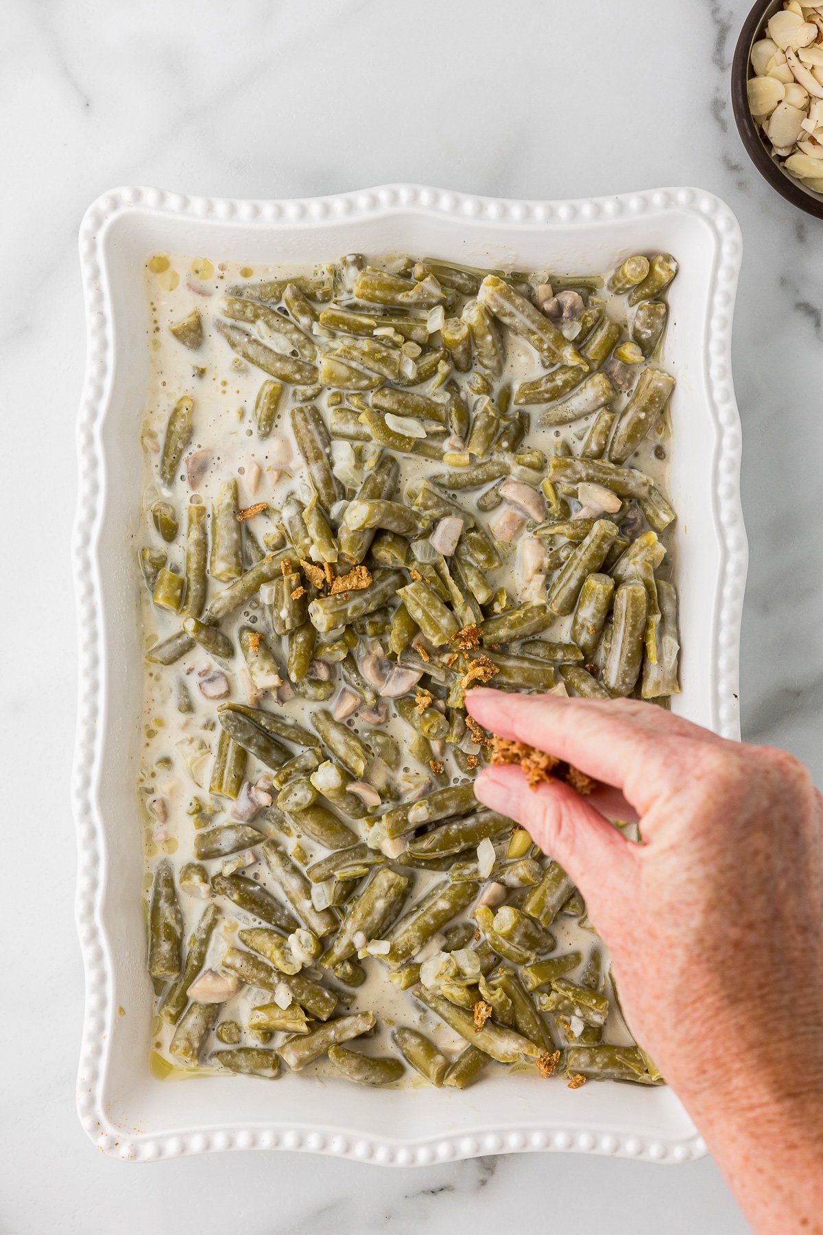 Almonds and onions being added to the top of the casserole.