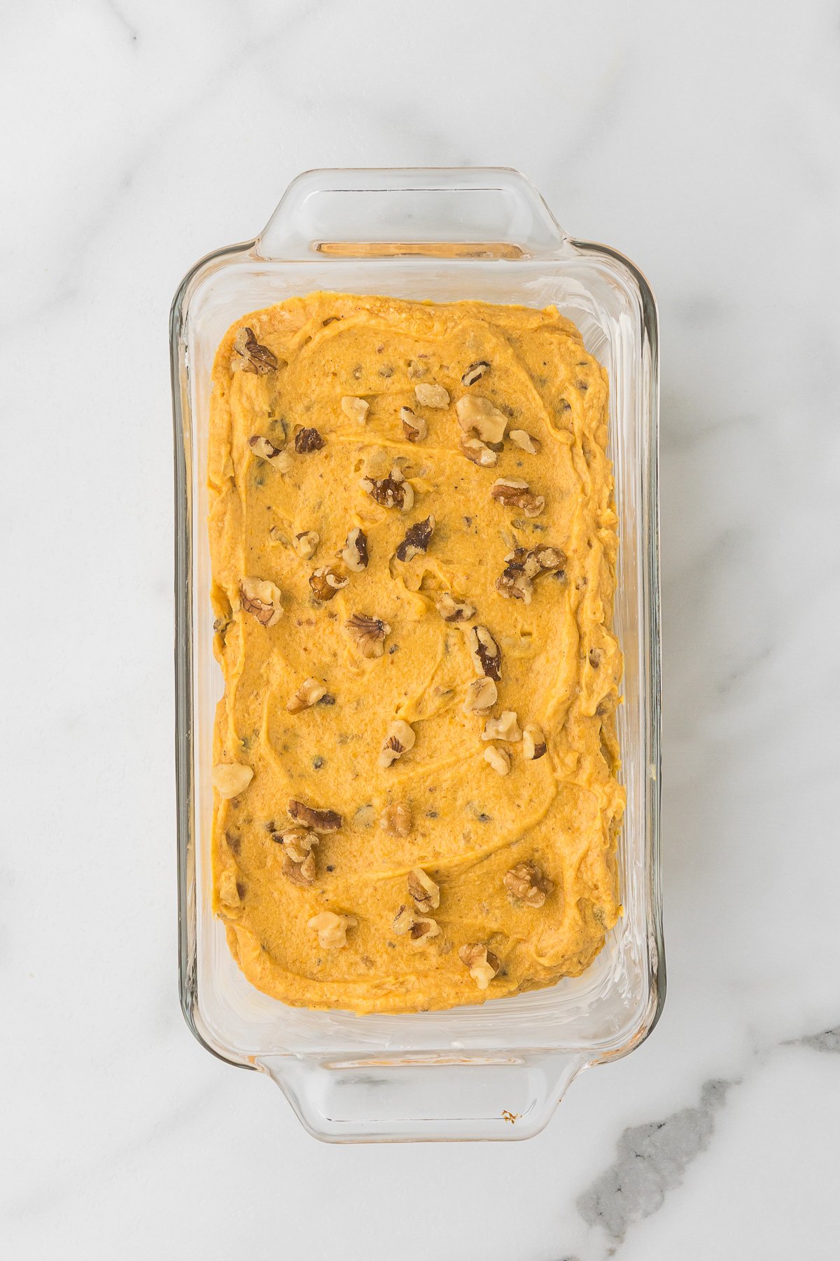A clear loaf pan with pumpkin batter added before baking.
