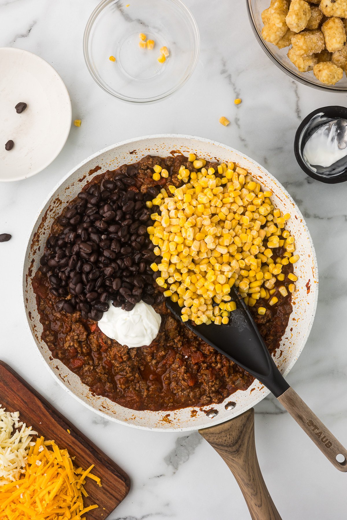 Sour cream, black beans and corn added to a white skillet with the sauce ingredients for taco mixture.