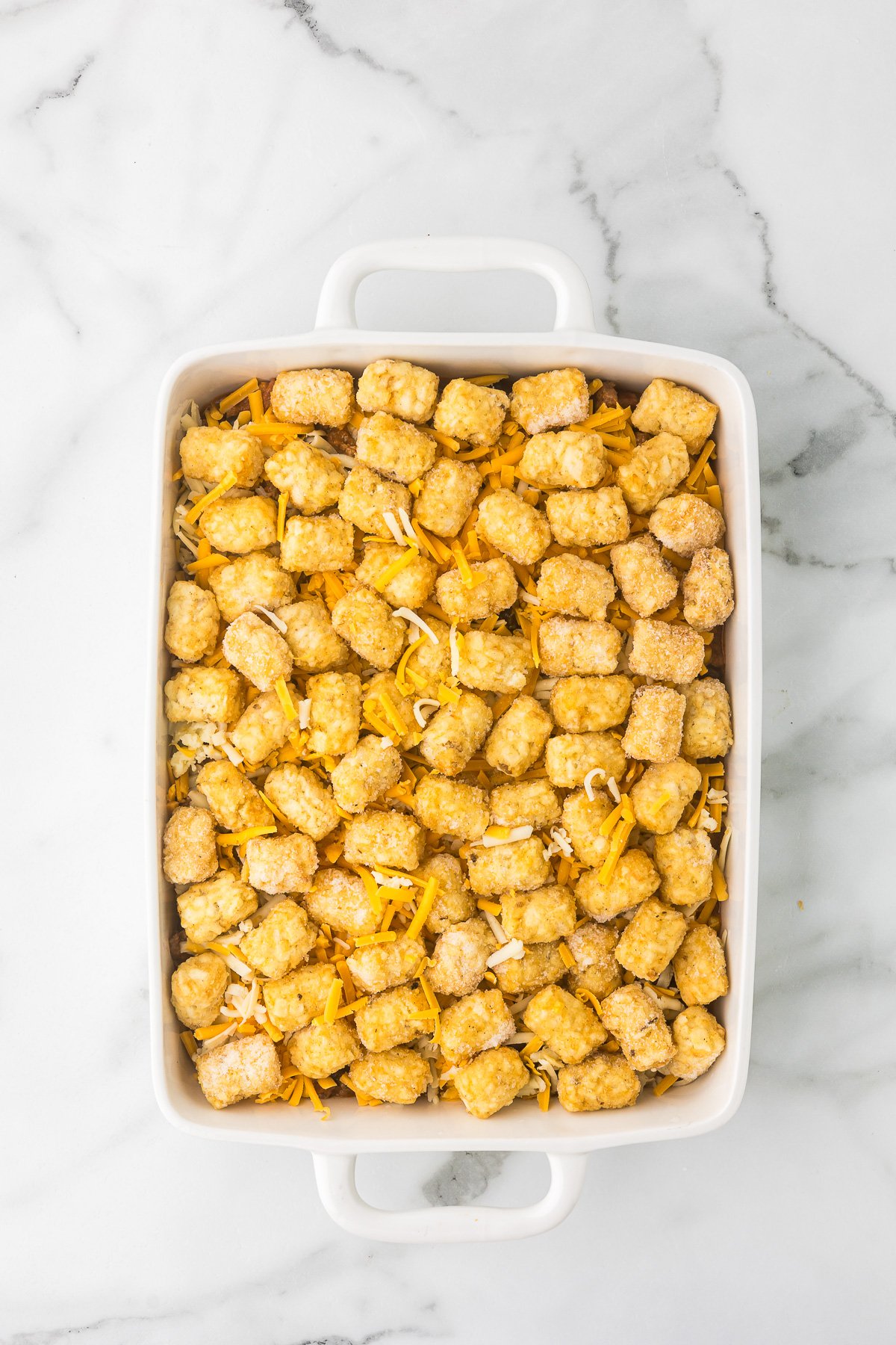 Tater tots added to the casserole dish before baking taco tater tot casserole.