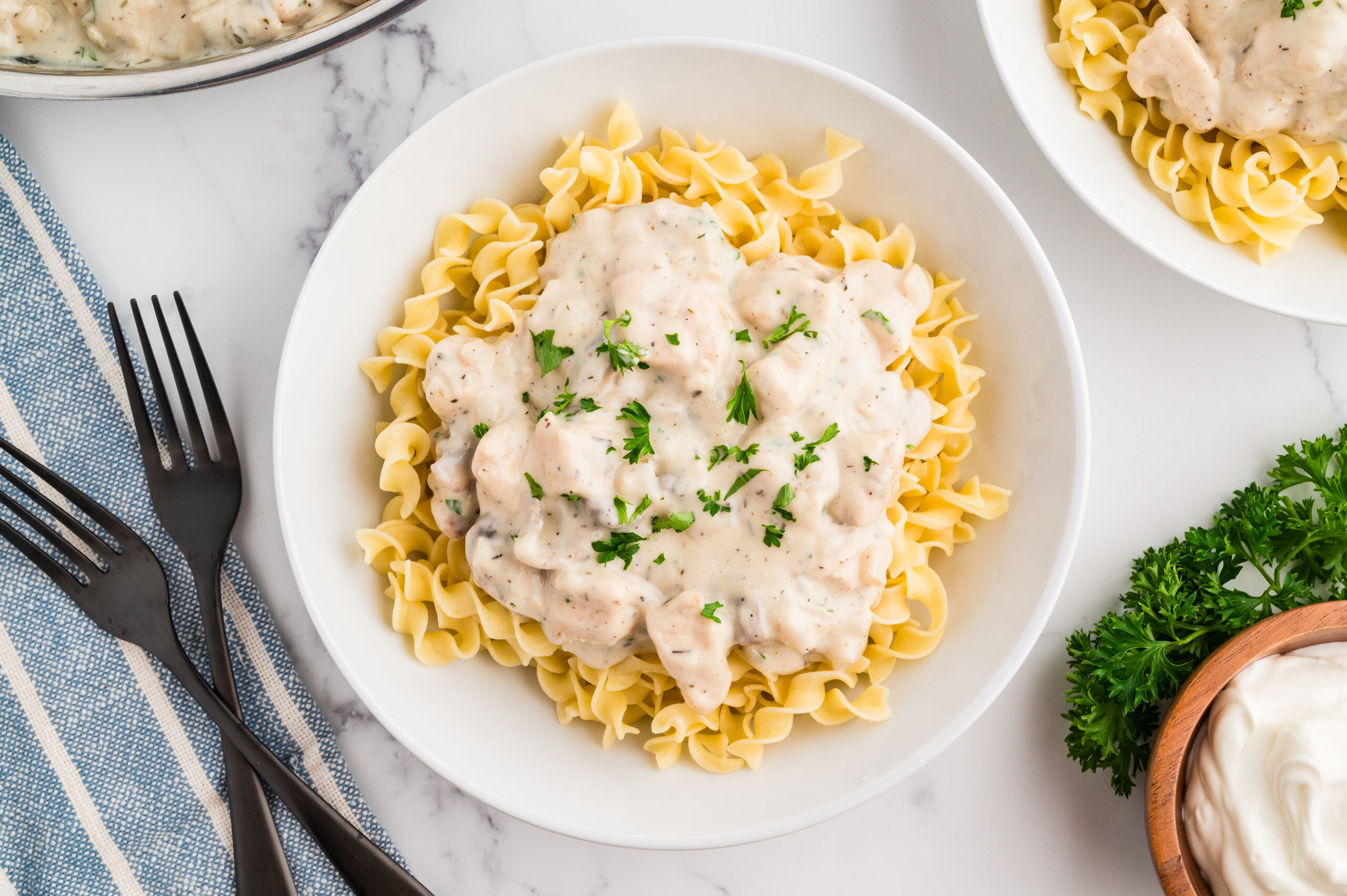 Chicken Stroganoff served over egg noodles in a white bowl with chopped parsley as garnish.