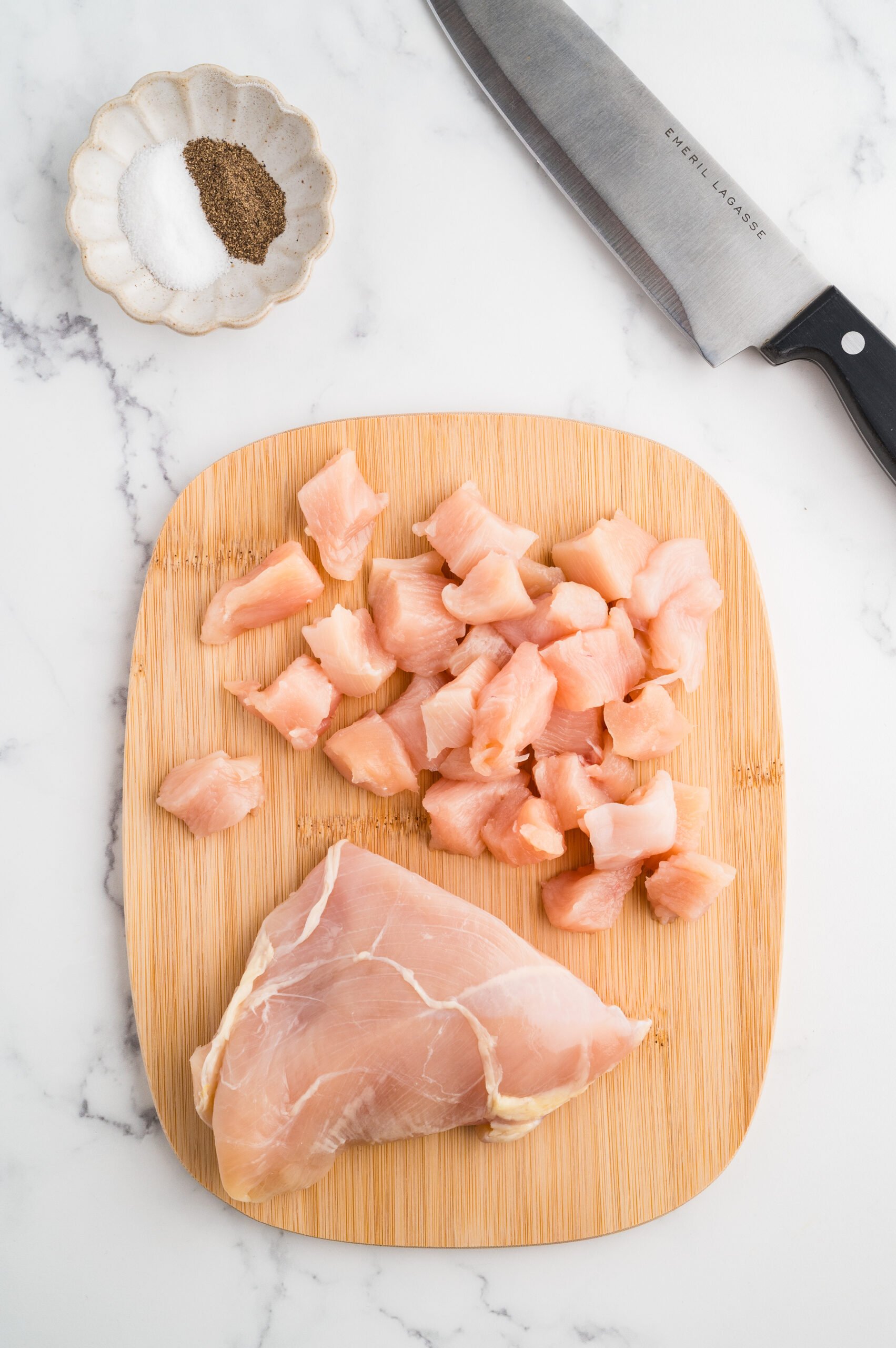 Chicken diced on a cutting board with a knife and salt and pepper on the side.