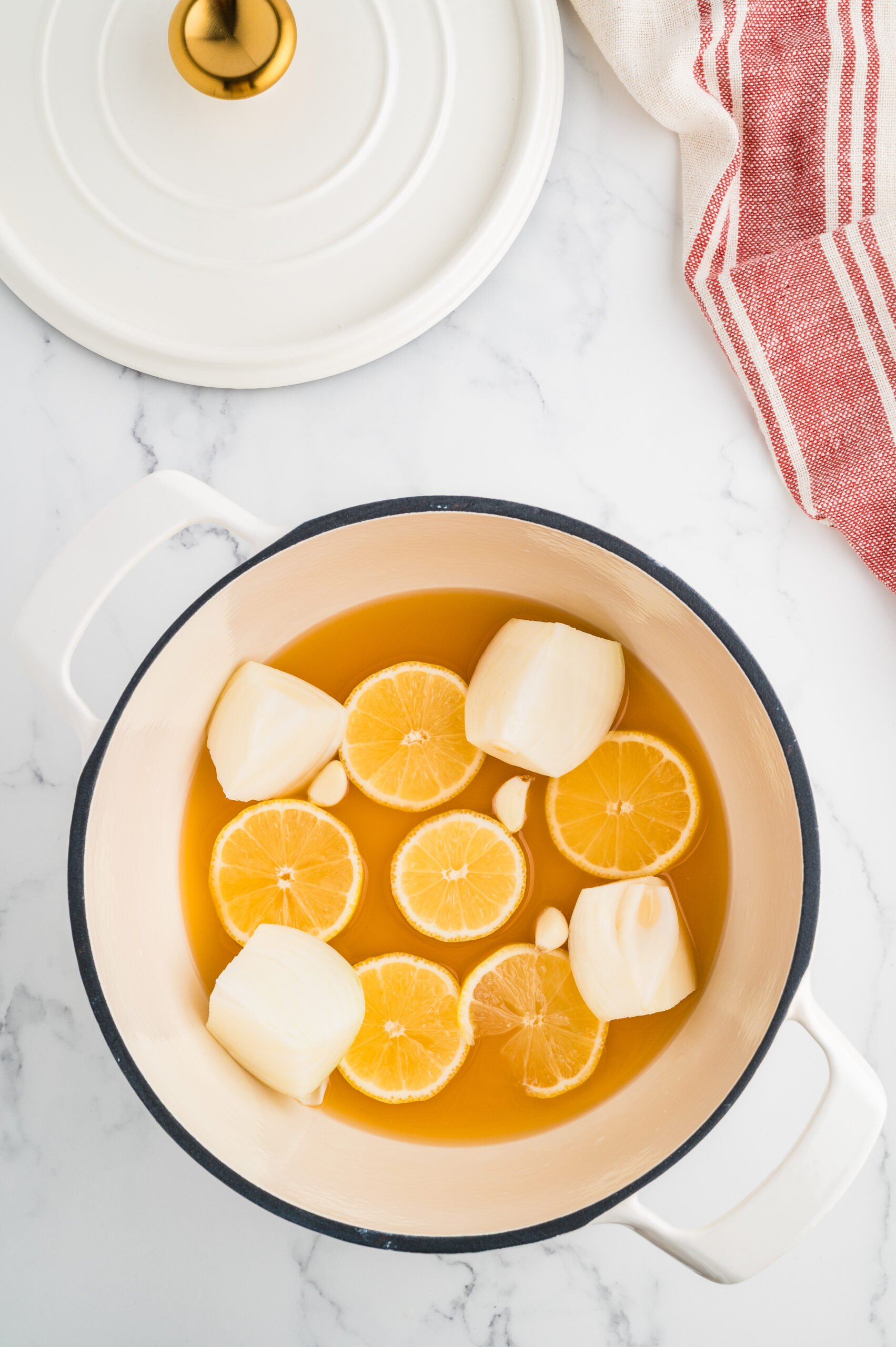 Dutch oven with broth, lemon slices, onion chunks, and whole garlic cloves before adding turkey.
