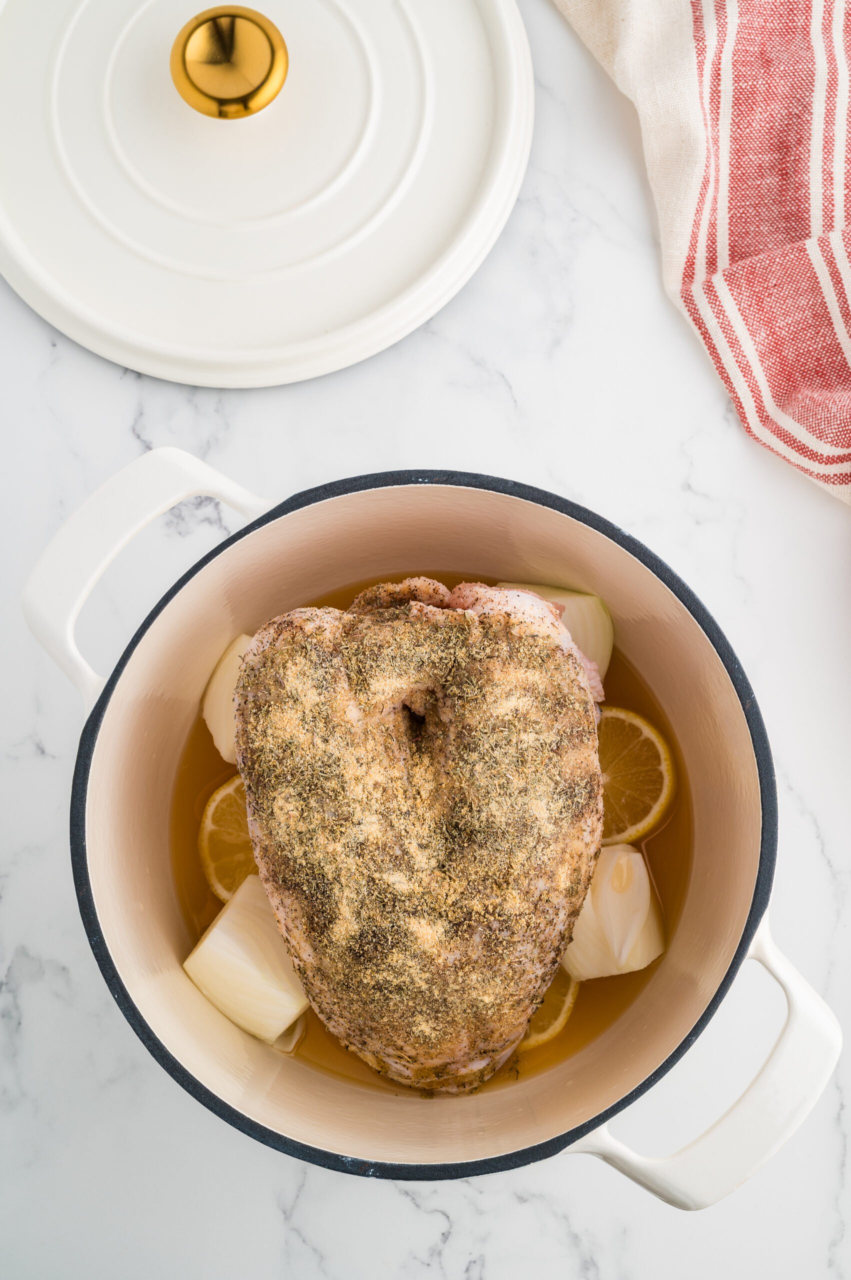 Seasoned bone-in turkey breast set over lemon, onion, and garlic in a Dutch oven, ready to roast