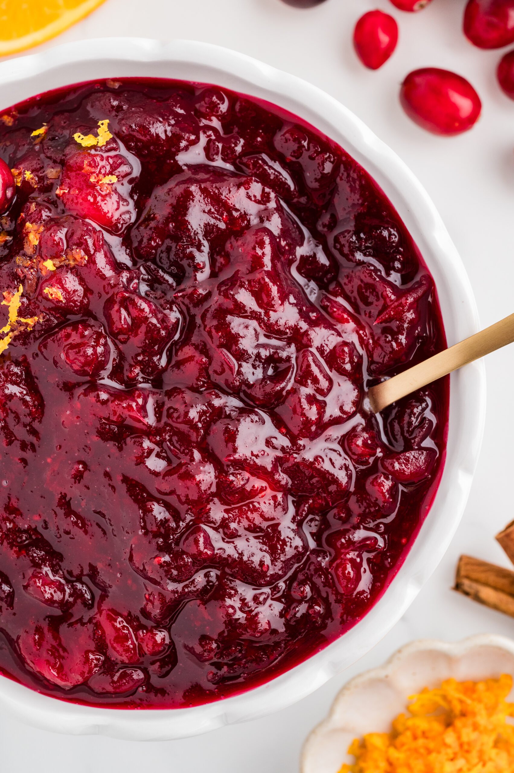 Bowl of whole berry cranberry sauce with orange slices, cinnamon sticks, and extra cranberries on top.