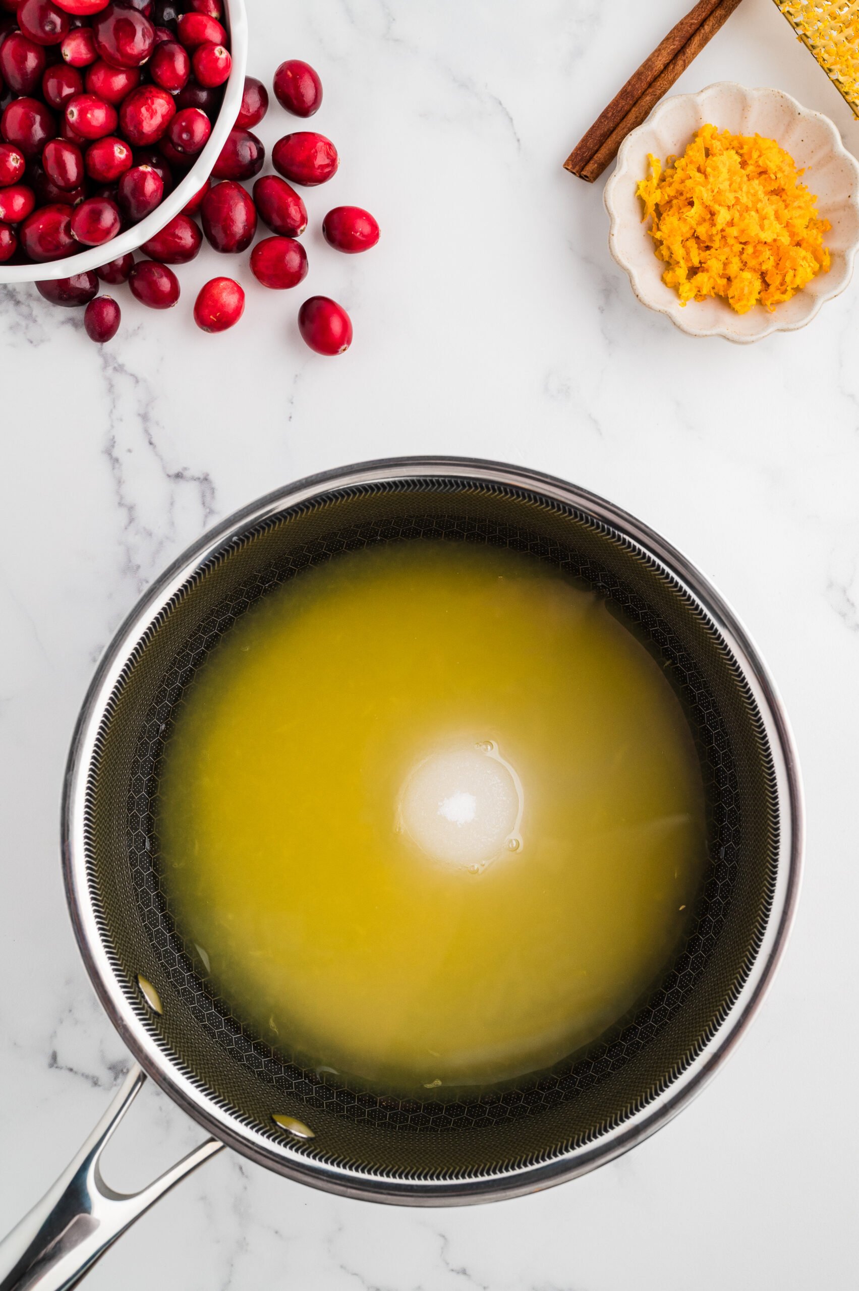 Saucepan with orange juice, water, and sugar heating together as the base for fresh cranberry sauce.
