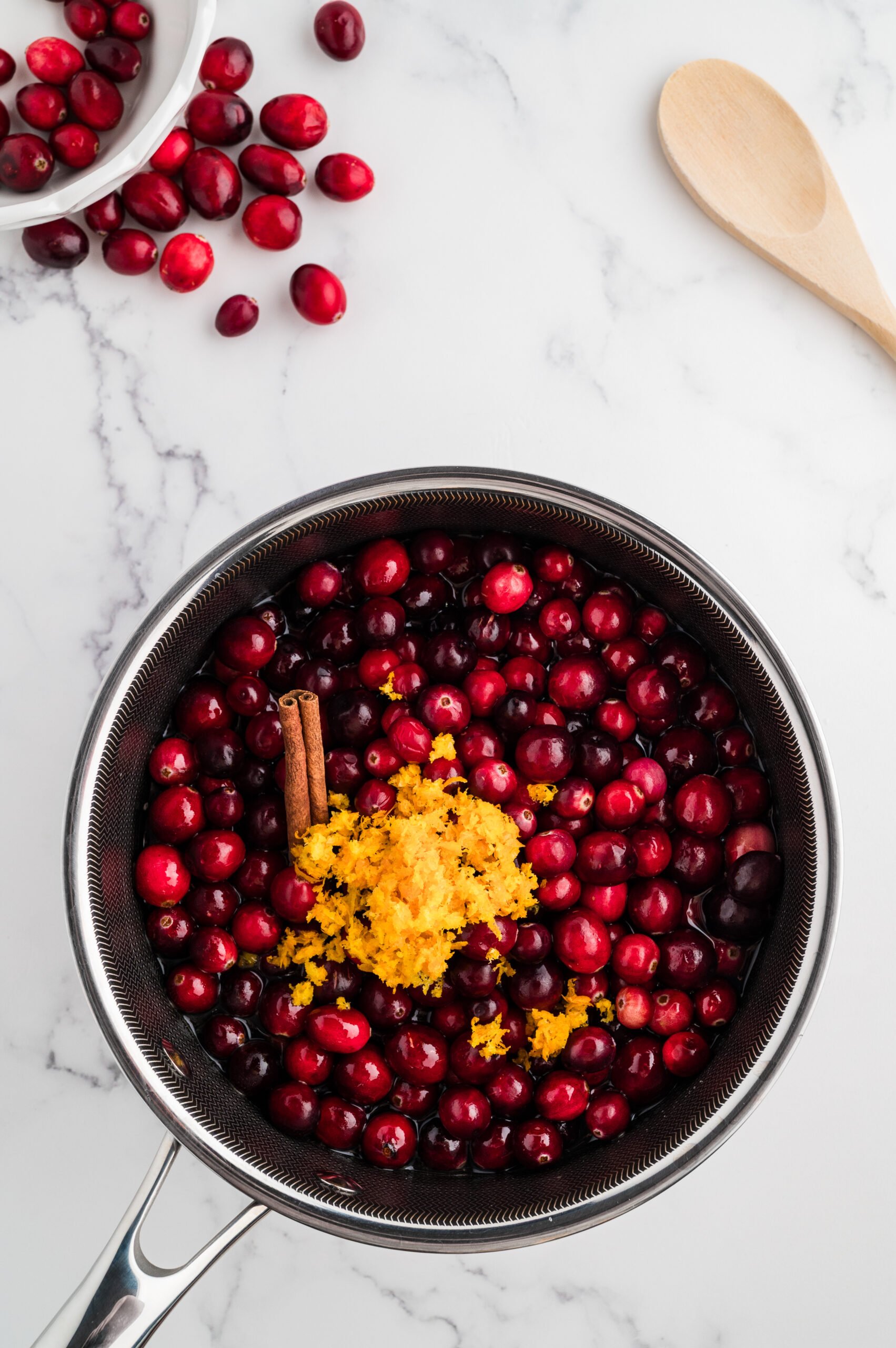 Fresh cranberries, orange zest, and cinnamon sticks added to the saucepan to cook whole berry cranberry sauce.