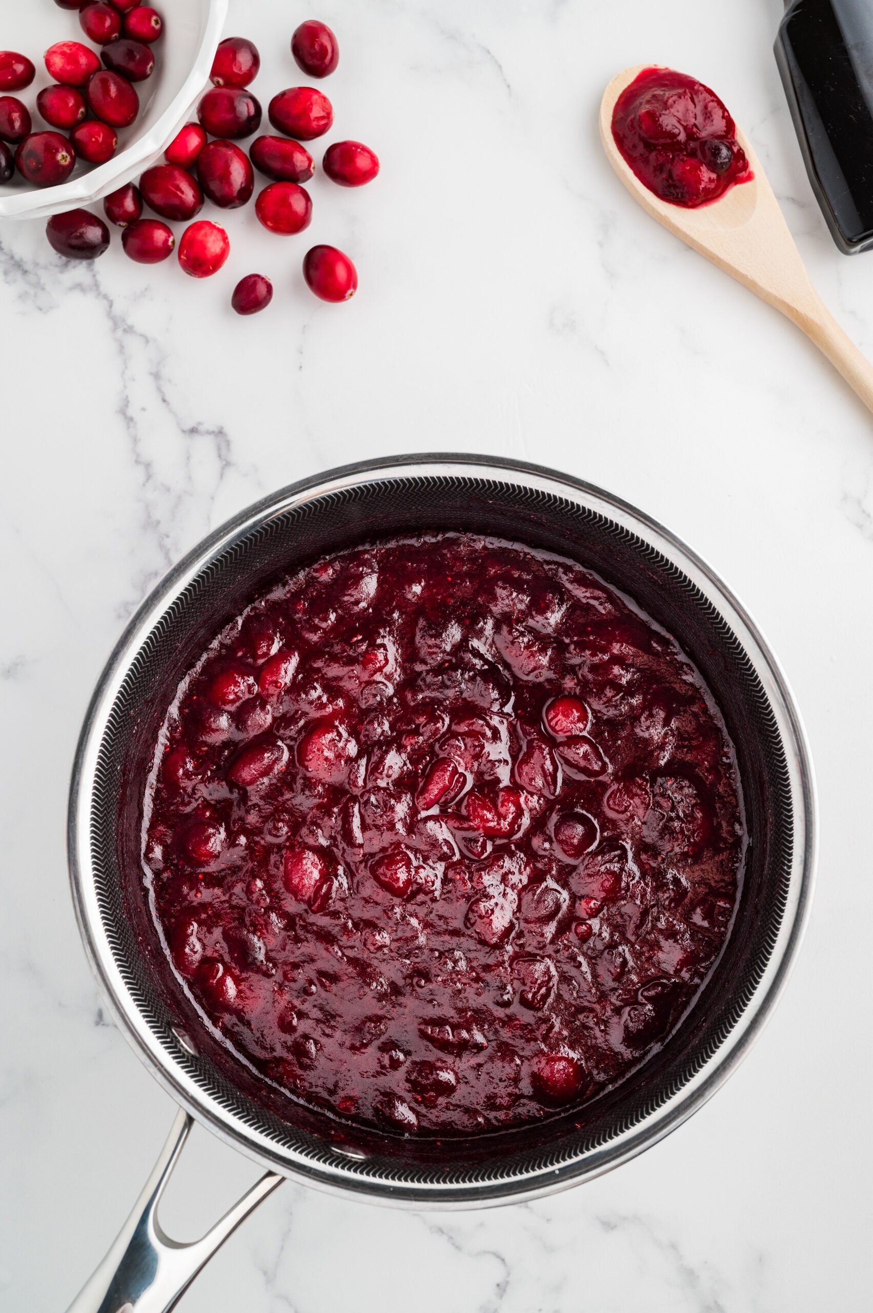 Thick, jammy whole berry cranberry sauce finished cooking in a saucepan on a marble surface.