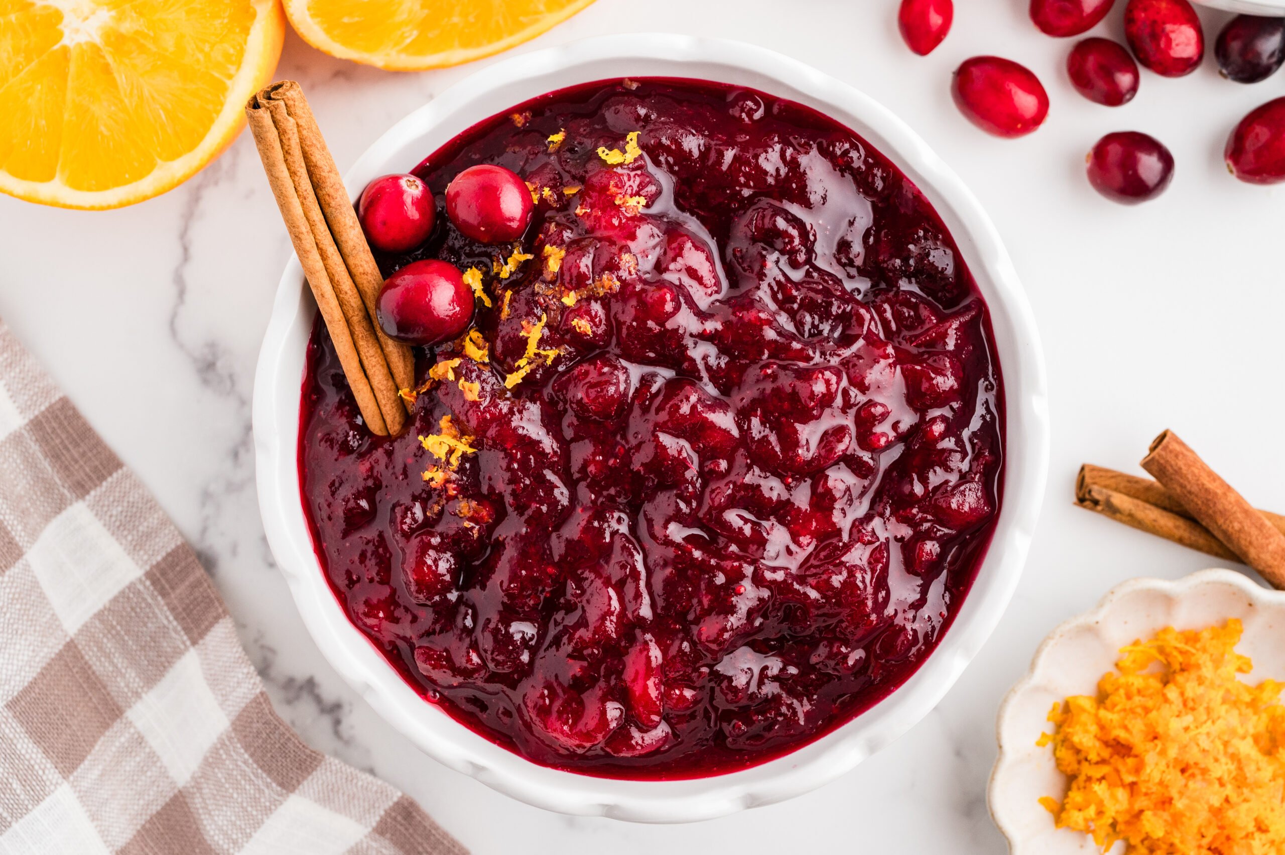 Bowl of whole berry cranberry sauce garnished with orange zest, fresh cranberries, and cinnamon sticks.
