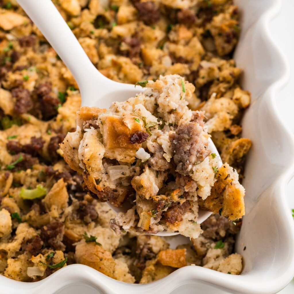 Serving spoon lifting a scoop of baked sourdough sausage stuffing with golden toasted edges.