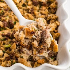 Serving spoon lifting a scoop of baked sourdough sausage stuffing with golden toasted edges.