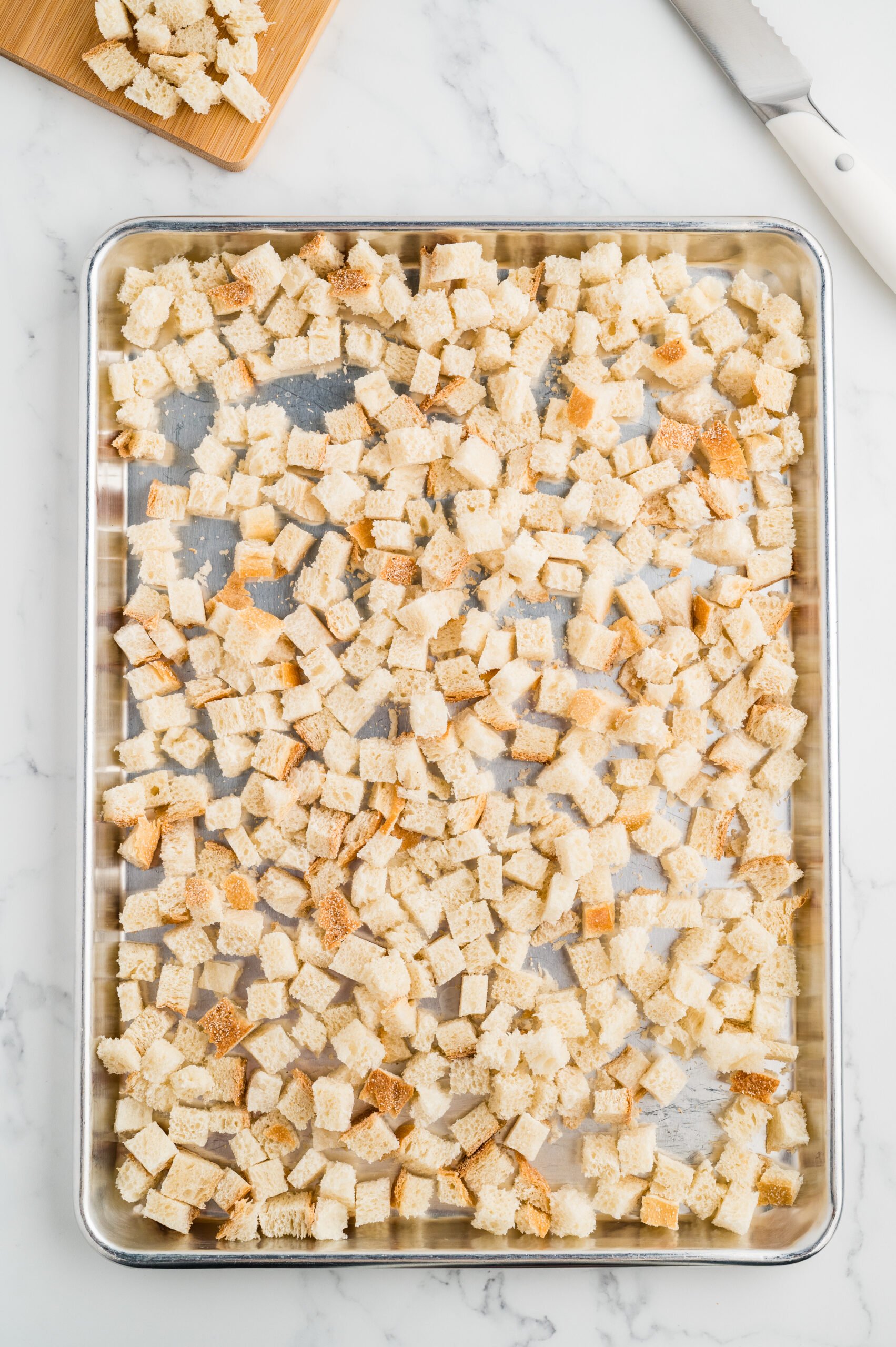 Half-inch sourdough bread cubes spread on a sheet pan to dry for stuffing.