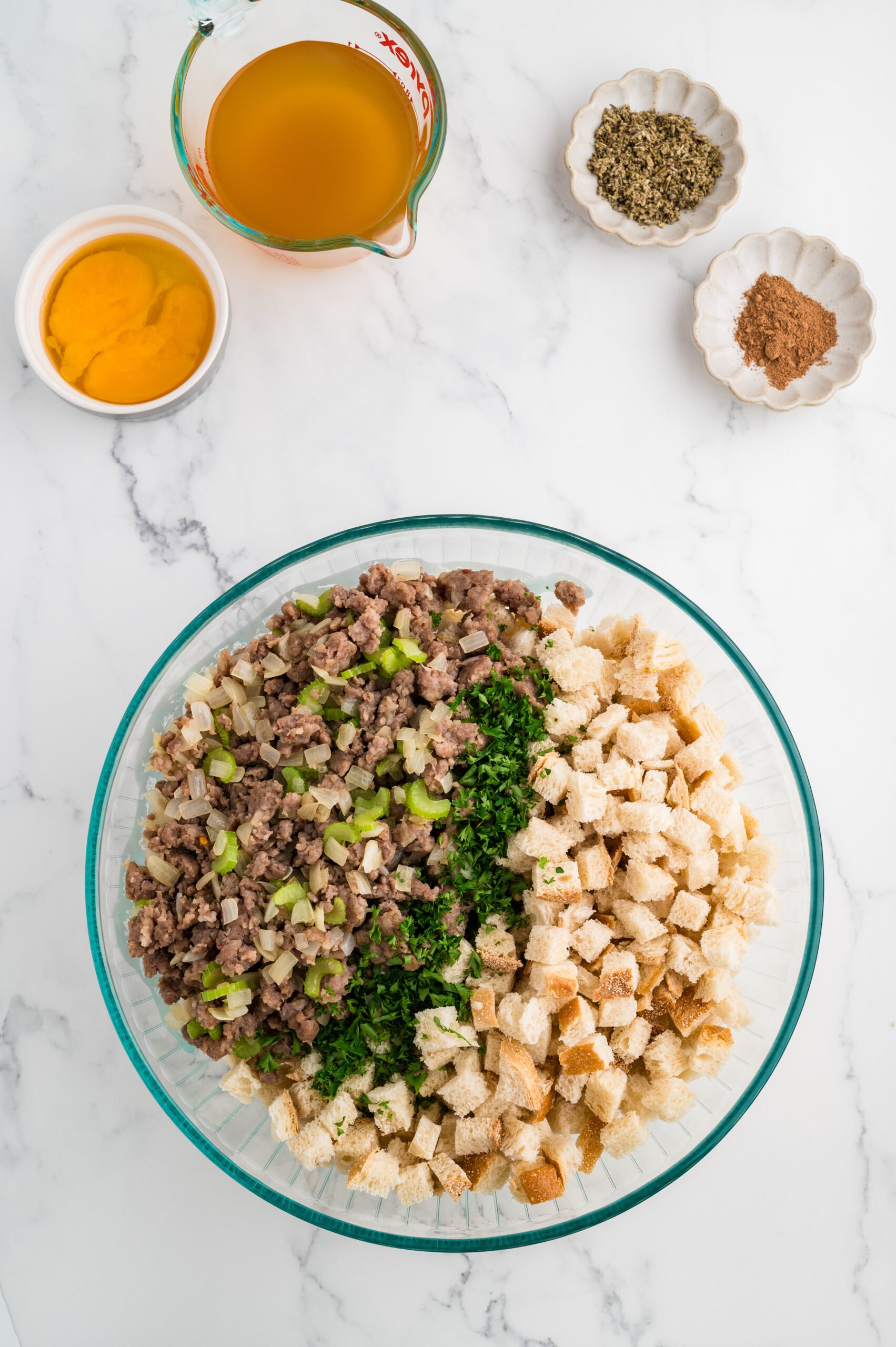 Large mixing bowl filled with dried sourdough cubes, cooked sausage, onion, celery, and fresh parsley for stuffing.
