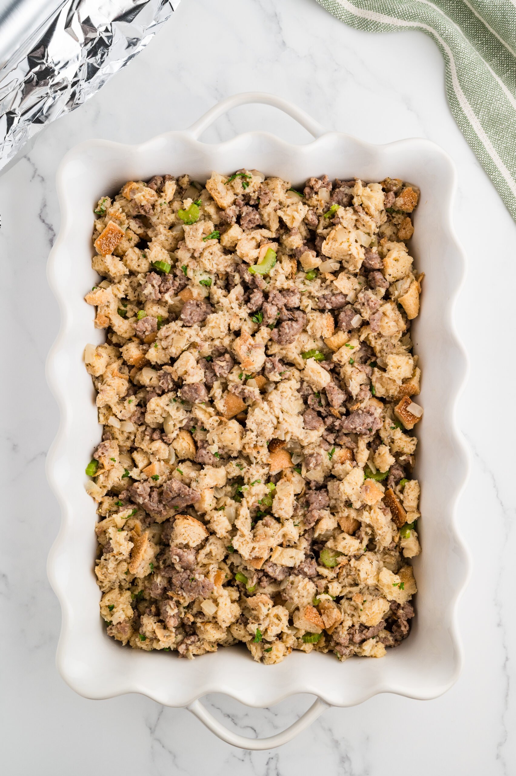 Sourdough and sausage stuffing packed into a white 9×13 baking dish ready to bake at 375 degrees.